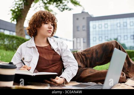 Femme aux cheveux bouclés s'engage dans le travail indépendant à l'extérieur, entouré d'une végétation luxuriante. Banque D'Images