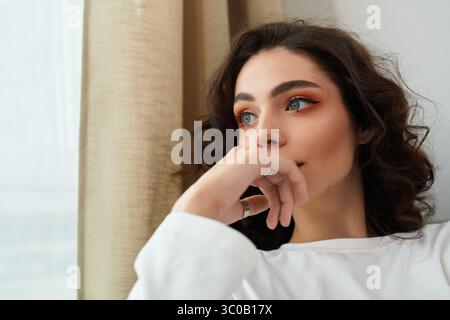 Une belle jeune femme se détend dans son appartement élégant tout en perdant dans ses pensées. Banque D'Images