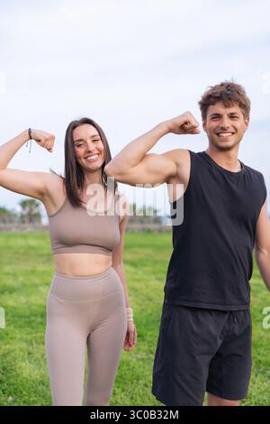 Young fit couple fléchir les bras et sourire pendant l'entraînement en plein air dans le parc balnéaire Banque D'Images