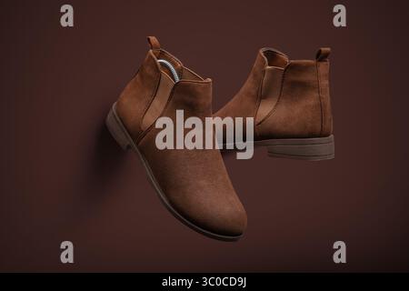 Vue de dessus d'une paire de bottes Chelsea modernes en daim marron placées en diagonale sur un fond marron assorti. La disposition minimaliste et la texture élégante hig Banque D'Images