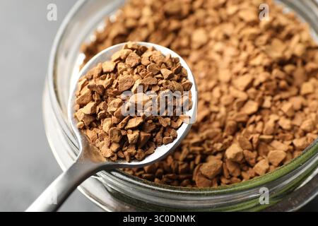 Cuillère avec café instantané granulé et pot sur fond gris, gros plan Banque D'Images