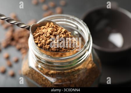 Cuillère avec café instantané granulé et pot sur la table sombre, gros plan Banque D'Images