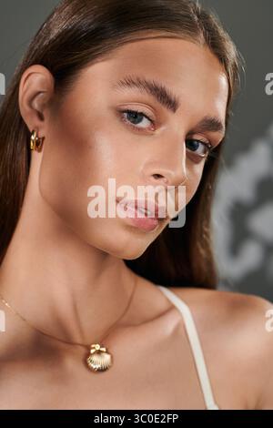 Une jeune femme à la peau bronzée met en valeur sa beauté naturelle tout en posant sur un fond gris. Banque D'Images