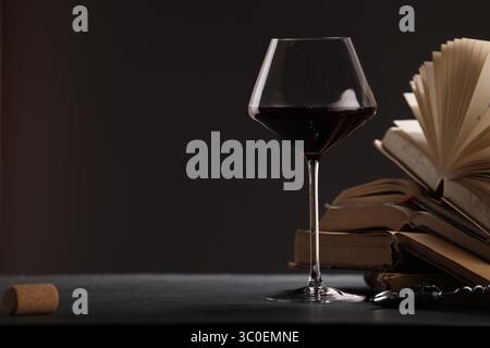 Vin rouge en verre et livres sur table texturée grise sur fond sombre, gros plan. Espace pour le texte Banque D'Images