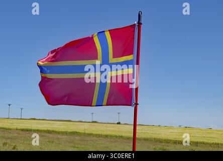 Drapeau rouge avec croix jaune ondulant devant le ciel bleu et prairie fleurie, drapeau des îles Orcades, continentale, îles Orcades, Écosse, Great BRI Banque D'Images