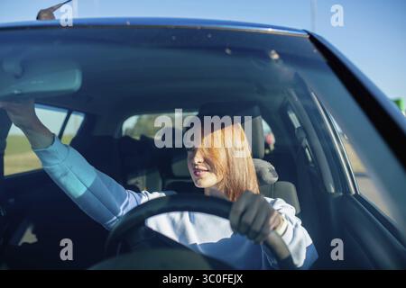 Femme confiante conduisant une voiture sous un ciel bleu ensoleillé Banque D'Images