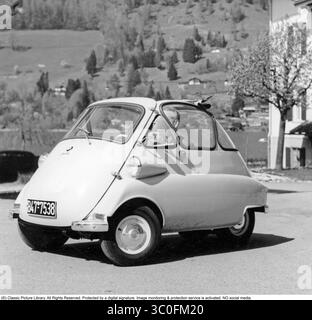 Conduite dans les années 1950 BMW Isetta, 1955. Capturée dans une photographie de 1955, la BMW Isetta, une microvoiture originale avec un design distinctif en forme d'œuf et une porte à ouverture frontale, a été une sensation d'après-guerre. Propulsé par un moteur monocylindre de 247 cm3 produisant 12 chevaux, il atteint une vitesse de pointe d'environ 85 km/h. Populaire en milieu urbain, l'Isetta a aidé BMW à relever les défis financiers dans les années 1950 Banque D'Images