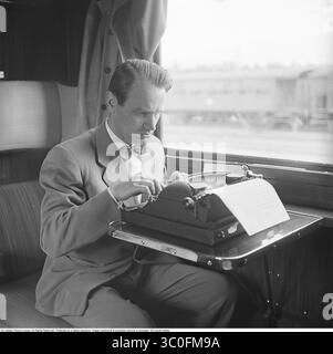 Karl-Gustaf Kristoffersson, 1918-2011, photographe suédois légendaire connu pour ses innombrables reportages photographiques emblématiques dans tous les grands magazines suédois et internationaux. Ici 1950, en voyage de reportage à Karlstad pour le magazine hebdomadaire *Vecko-Revyn*. À cette époque, il avait été chargé de trouver la plus belle suédoise pour représenter la Suède dans le concours de beauté Miss Europe. Avec sa machine à écrire portable, il écrit des articles assis dans un compartiment de train. Kristoffersson réf. AY69-1 Banque D'Images