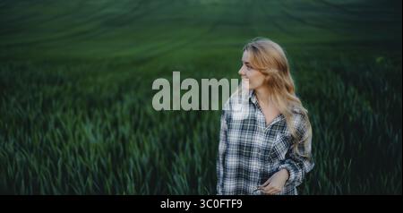 Femme dans une chemise à carreaux se tient dans un champ vert luxuriant, entouré par une nature sereine Banque D'Images