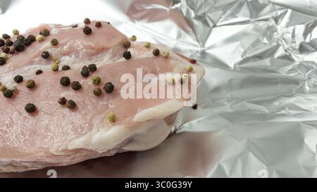 un morceau de viande de porc crue avec des pois de poivre sur papier d'aluminium est préparé pour la cuisson en gros plan Banque D'Images