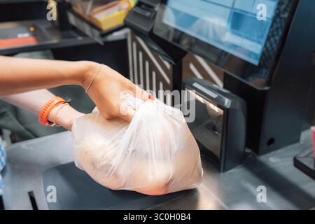 Main de femme tenant le sac en plastique avec la nourriture sur le scanner de code à barres à la caisse dans le supermarché Banque D'Images