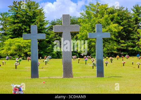 Trois croix de pierre verticales sont placées dans un cimetière tranquille avec des arrangements floraux colorés sous le ciel lumineux. Banque D'Images