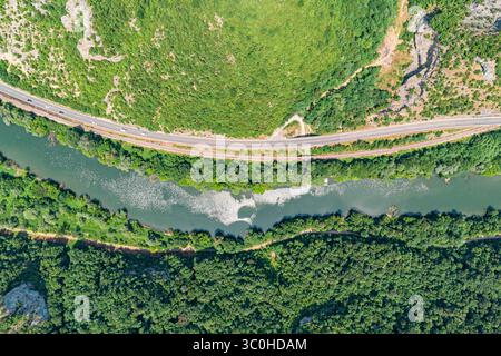 Capture d'une vue aérienne de voitures voyageant le long d'une autoroute à côté d'une rivière sinueuse et d'un chemin de fer, niché dans une vallée verdoyante avec des forêts Banque D'Images