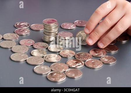 Mains d'enfant avec des pièces de monnaie sur fond gris, gros plan Banque D'Images