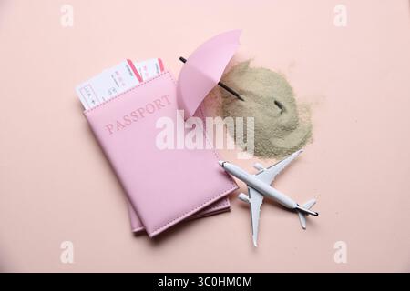Modèle d'avion, passeports, billets d'avion, sable et petit parapluie sur fond beige, plat Banque D'Images