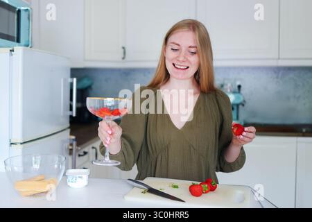 Création d'un parfait à la fraise, femme superposant des fruits et du yaourt dans un verre Banque D'Images