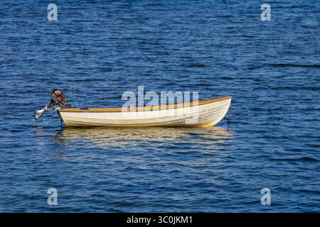 Un petit bateau à moteur repose calmement à la surface des eaux bleues, reflétant la lumière du soleil, entouré d'une atmosphère sereine. L'environnement suggère un calme Banque D'Images