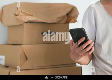 Femme vérifiant le téléphone tout en se tenant près d'une pile de colis. Propriétaire de petite entreprise gérant des commandes en ligne ou recevant des livraisons. E-commerce, expédition Banque D'Images