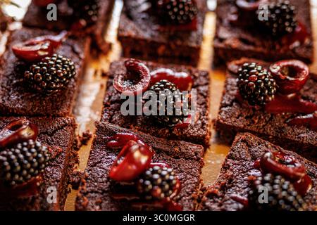 Gros plan de riches brownies au chocolat recouverts de cerises fraîches et de mûres. Un éclairage chaud améliore la texture du dessert. Banque D'Images