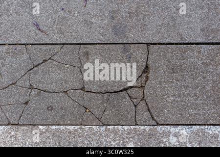 Vue de haut en bas d'un carreau de chaussée en béton gris fissuré. Arrière-plan abstrait montrant la texture, les dommages et la décomposition urbaine. Banque D'Images
