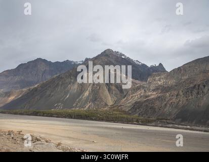 Paysage himalayen majestueux avec des pics arides, une végétation de contreforts et la trajectoire asséchée de la rivière Shyok dans le Ladakh, en Inde. Banque D'Images