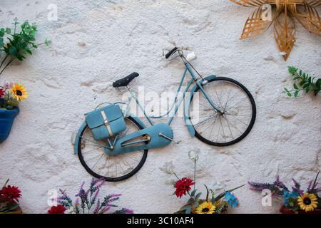 Installation artistique sur un mur de béton blanc avec un vélo vintage entouré de fleurs artificielles. Banque D'Images