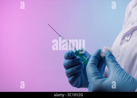 docteur tenant seringue avec vaccin et coton sur fond néon, gros plan. Vaccination, immunisation ou prévention des maladies contre la grippe ou le virus Banque D'Images