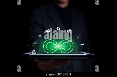 Homme d'affaires tenant la tablette avec le symbole de l'infini avec l'icône de l'environnement économique de cercle flottant et la lumière verte. Croissance durable future des investissements, Banque D'Images