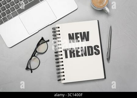 Nouvelles tendances inscription dans le cahier, ordinateur portable, café, verres et stylo sur la table grise, vue de dessus Banque D'Images