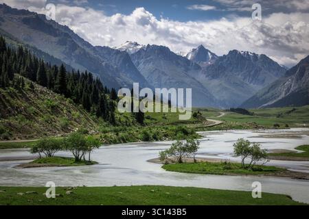 Vue sur la rivière sinueuse reflétant le ciel, flanquée de prairies verdoyantes et de montagnes imposantes recouvertes de neige, Karakol, Kirghizistan. Banque D'Images