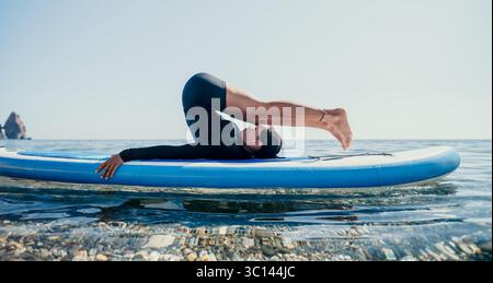 Yoga Paddleboard Ocean Man pratiquant le yoga sur une planche de paddleboard dans l'océan pour la remise en forme. Banque D'Images