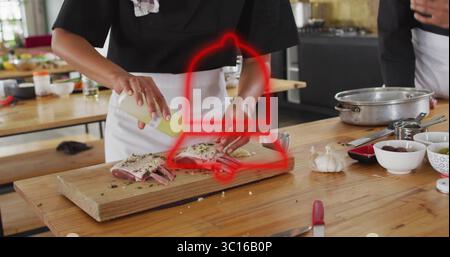 Chef dans un tablier blanc sauce arrosante sur grille d'agneau sur la table dans la cuisine à l'aide d'un flacon souple Banque D'Images