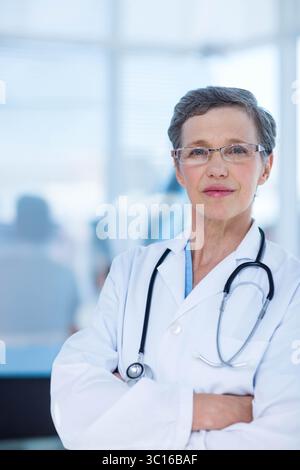 Médecin senior portant une blouse de laboratoire et des lunettes debout dans le couloir de l'hôpital avec stéthoscope Banque D'Images