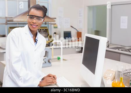 Femme afro-américaine portant une blouse de laboratoire dactylographiant sur le clavier au poste de travail du laboratoire de chimie, espace de copie Banque D'Images