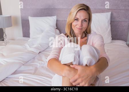 Femme assise sur le lit serrant les genoux dans la chambre avec lampe décorative par table de chevet métallique Banque D'Images