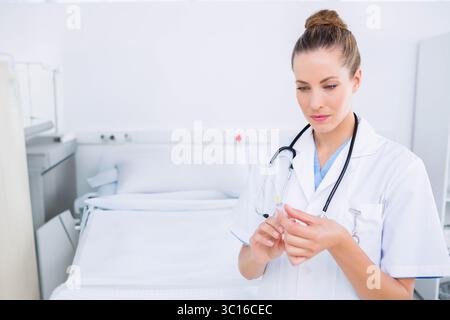 Infirmière préparant la seringue dans la chambre d'hôpital près du lit et de l'armoire, portant un manteau blanc, espace de copie Banque D'Images