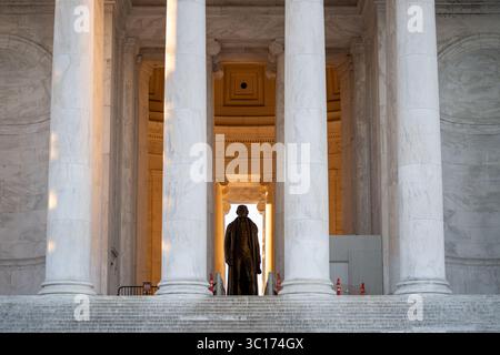 Jefferson Memorial Statue Washington DC // WASHINGTON DC — la statue en bronze de Thomas Jefferson est visible à travers les colonnes du portique nord du Jefferson Memorial, avec la lumière dorée du soleil illuminant la salle principale juste après le lever du soleil. La statue de 5,8 mètres, créée par le sculpteur Rudulph Evans, représente le troisième président des États-Unis et l'auteur principal de la Déclaration d'indépendance. Le Jefferson Memorial, achevé en 1943, a été conçu par l'architecte John Russell Pope dans le style néoclassique avec une colonnade circulaire de colonnes ioniques. Le mémorial se trouve sur le Tidal Basin et Banque D'Images