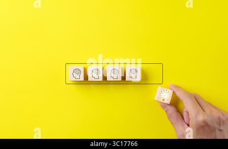 Idée créative et concept d'innovation de connaissance. Main met des blocs en bois, cube avec icône d'ampoule et divers humains ensemble sur fond jaune. Banque D'Images
