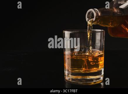 Bouteille de whisky verser dans un verre avec de la glace Banque D'Images