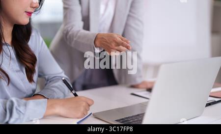 Femme asiatique professionnelle apprend prend des notes dans un bureau moderne. Un collègue expérimenté fournit des conseils lors d'une discussion d'affaires collaborative. Banque D'Images
