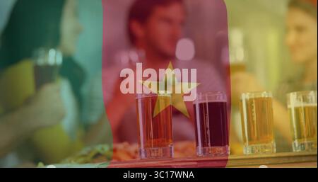 Amis toast avec quatre verres à bière sur la pagaie dans un pub sous le drapeau camerounais, avec plat à pizza Banque D'Images