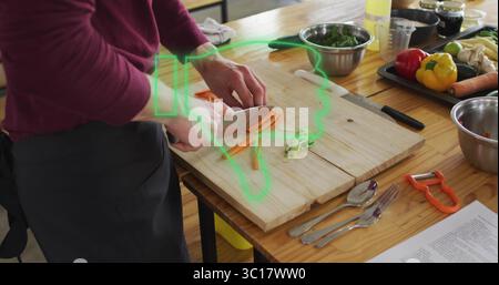 Homme hachant portant tablier tranchant des carottes et des oignons avec couteau à la table de préparation de la cuisine, copiez l'espace Banque D'Images