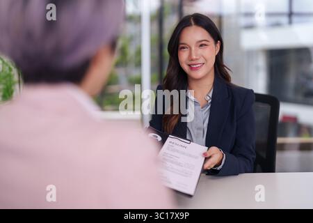Femme asiatique souriante présente son CV lors d'un entretien d'embauche professionnel. Elle semble confiante et prête pour de nouvelles perspectives de carrière. Banque D'Images