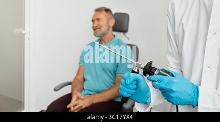 Médecin oto-rhino-laryngologiste tenant un vidéo-endoscope pour le contrôle endoscopique des organes ORL avant la procédure d'examen d'un homme âgé assis sur un fauteuil ORL Banque D'Images