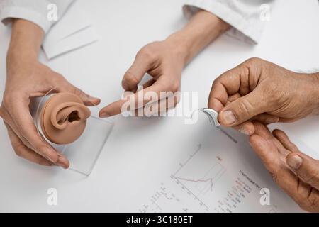 Le patient consulte un médecin au sujet du choix d'une prothèse auditive derrière l'oreille et discute de l'ajustement et des caractéristiques. Audiologie Banque D'Images
