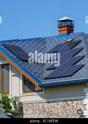 Une maison élégante dispose de plusieurs panneaux solaires installés sur son toit en bardeaux bleus, soulignant la consommation d'énergie propre Banque D'Images