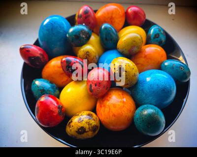 Un bol festif d'œufs de Pâques de caille colorés et peints à la main dans des tons de bleu et de rouge, représentant une tradition de vacances délicate et gourmande. Banque D'Images