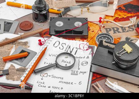 Espace de travail créatif sur le thème OSINT avec des outils vintage, des notes manuscrites et des éléments de presse sur une table grunge. Accessoires thématiques, pose à plat, gros plan Banque D'Images
