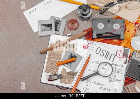Espace de travail créatif sur le thème OSINT avec des outils vintage, des notes manuscrites et des éléments de presse sur une table grunge. Accessoires thématiques, plat, vue de dessus Banque D'Images