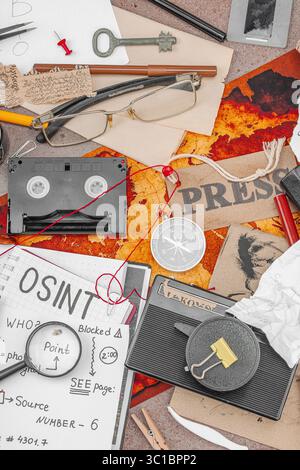 Espace de travail créatif sur le thème OSINT avec des outils vintage, des notes manuscrites et des éléments de presse sur une table grunge. Accessoires thématiques, plat, vue de dessus Banque D'Images